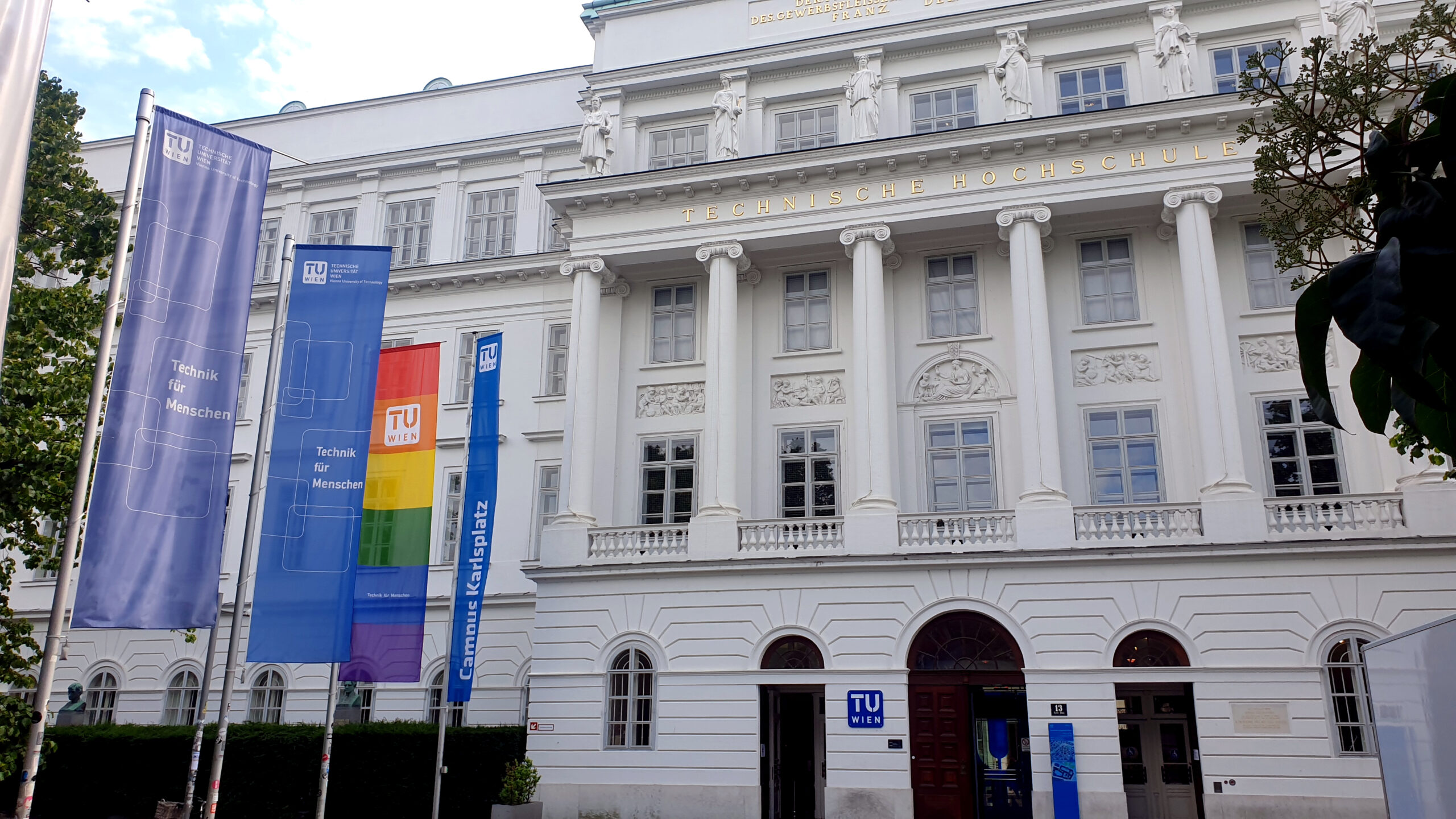 Das Hauptgebäude der TU Wien am Karlsplatz mit Regenbogenfahne im Vordergrund.